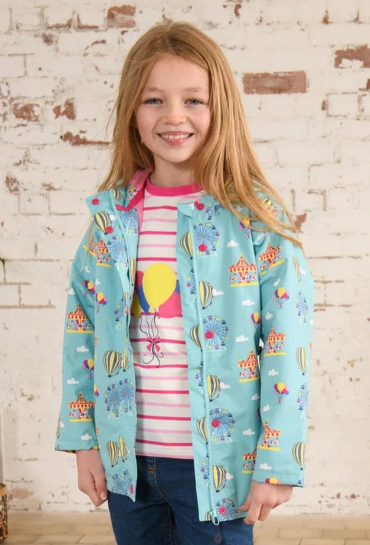 A child standing, wearing a blue waterproof jacket with a fairground/carnival print and a striped top underneath.