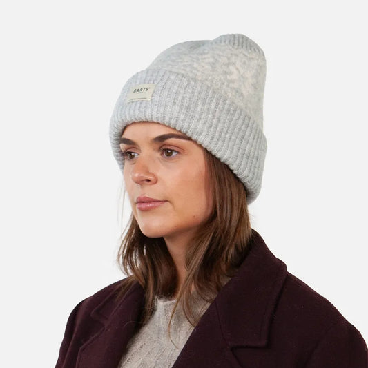 Woman wearing a grey Barts knitted Negomba beanie and dark coat on a white background