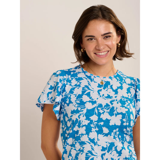 Close-up view of a woman wearing a Brakeburn short sleeve Ria blouse in blue with a white floral print.