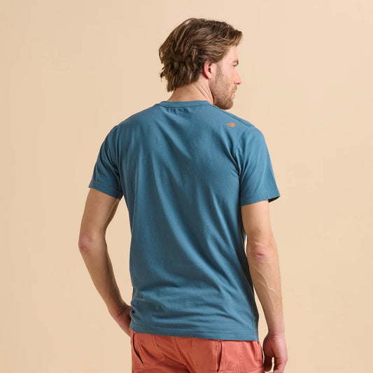 Back view of a man wearing a Brakeburn blue t-shirt on a beige background