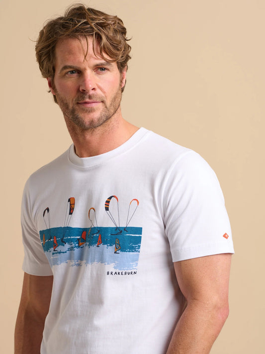 Man wearing a white Brakeburn Watersports t-shirt with a kite and windsurfer print design on a beige background