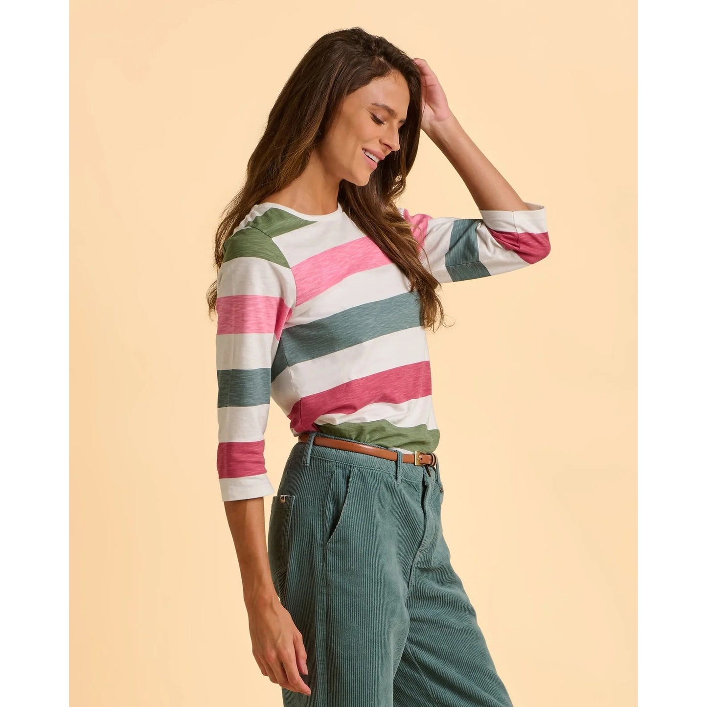 Woman wearing a colourful striped t-shirt and green pants on a beige background