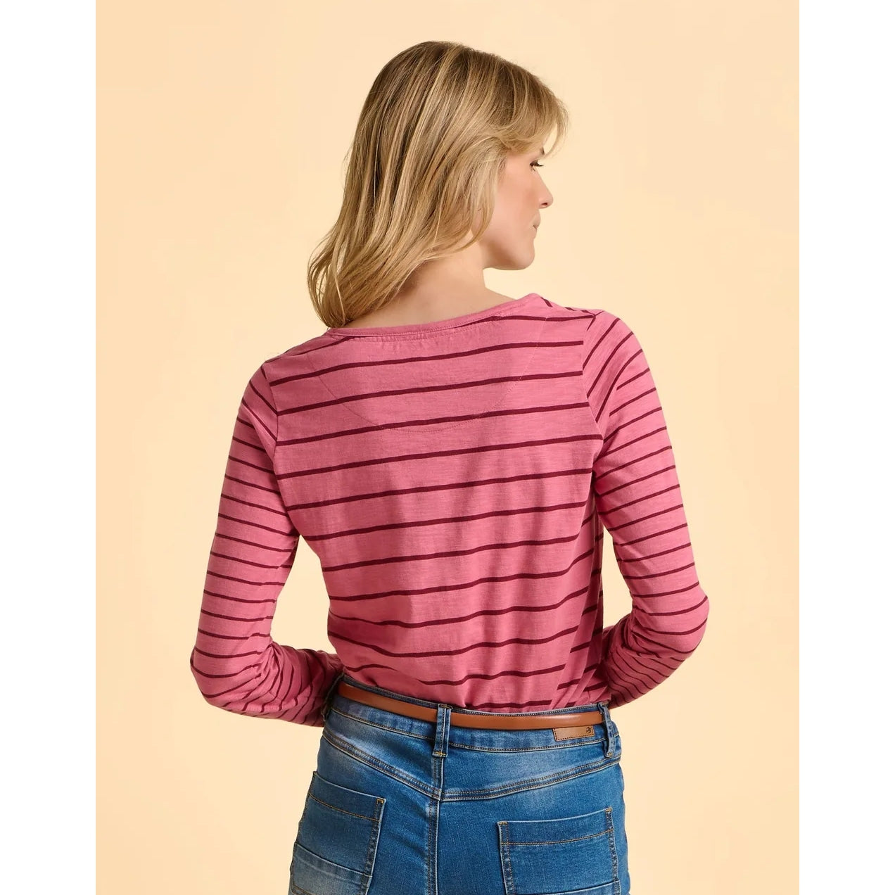 Woman wearing a pink striped long-sleeve shirt and blue jeans on a beige background