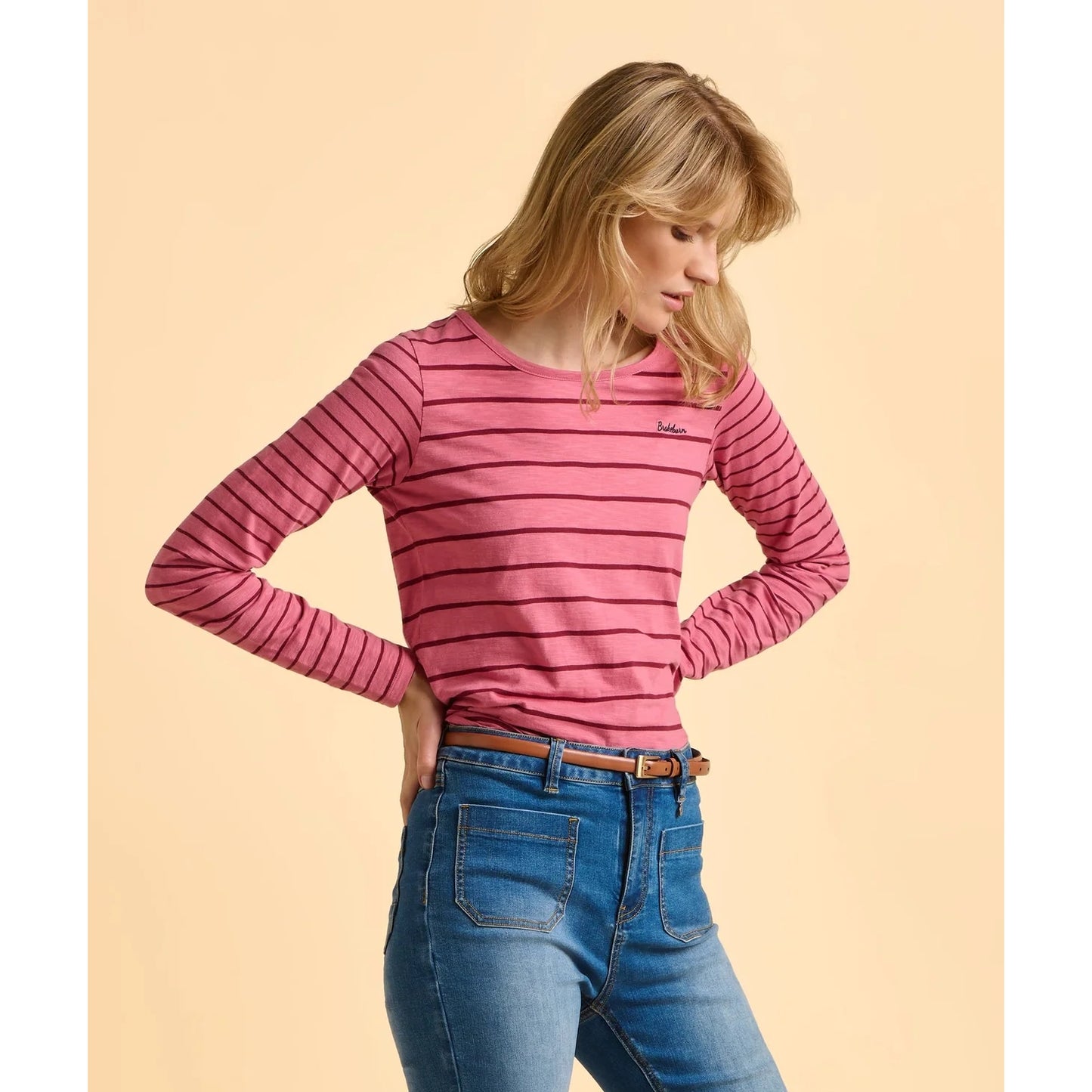 Woman wearing a pink striped long-sleeve top and blue jeans on a beige background