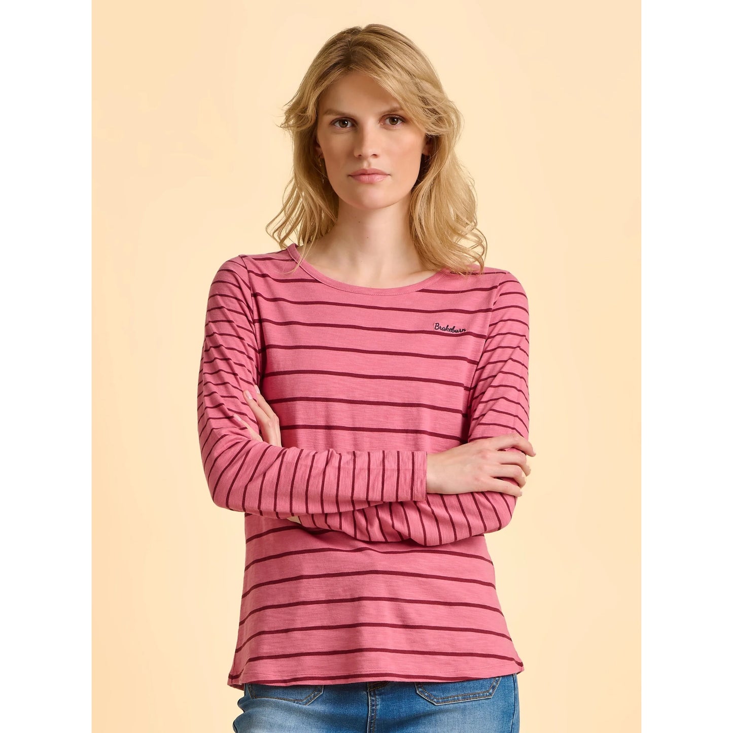 Woman wearing a pink striped shirt with a brand logo on a beige background