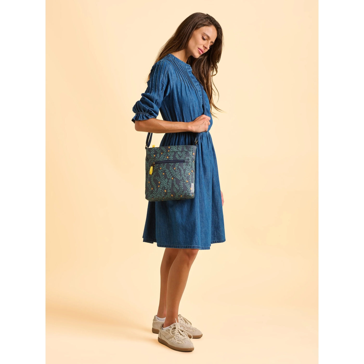 Woman in a blue dress wearing a Brakeburn Twilight Leaves cross body bag against a beige background