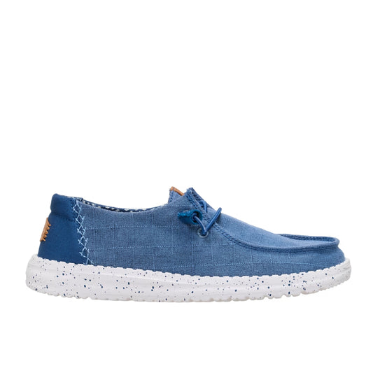 Side view of a women's Dude Wendy Chambray Grid shoe in Ensign Blue, featuring a white sole, matching blue elastic laces and decorative heel stitching.