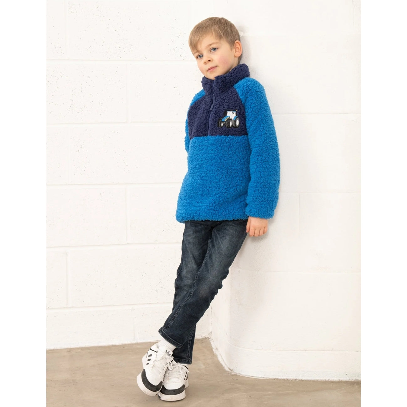 Child wearing a blue and navy Lighthouse Cadens fleece jumper against a white wall