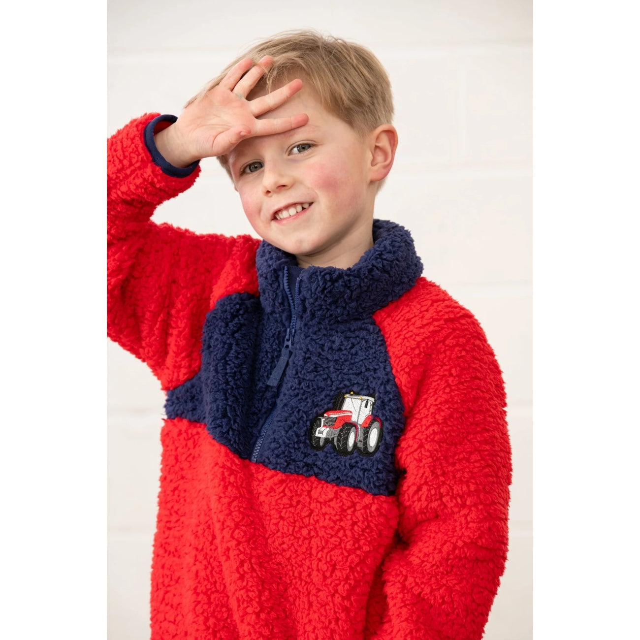 Child wearing a red Lighthouse Caden fleece jumper featuring a tractor design on a white background