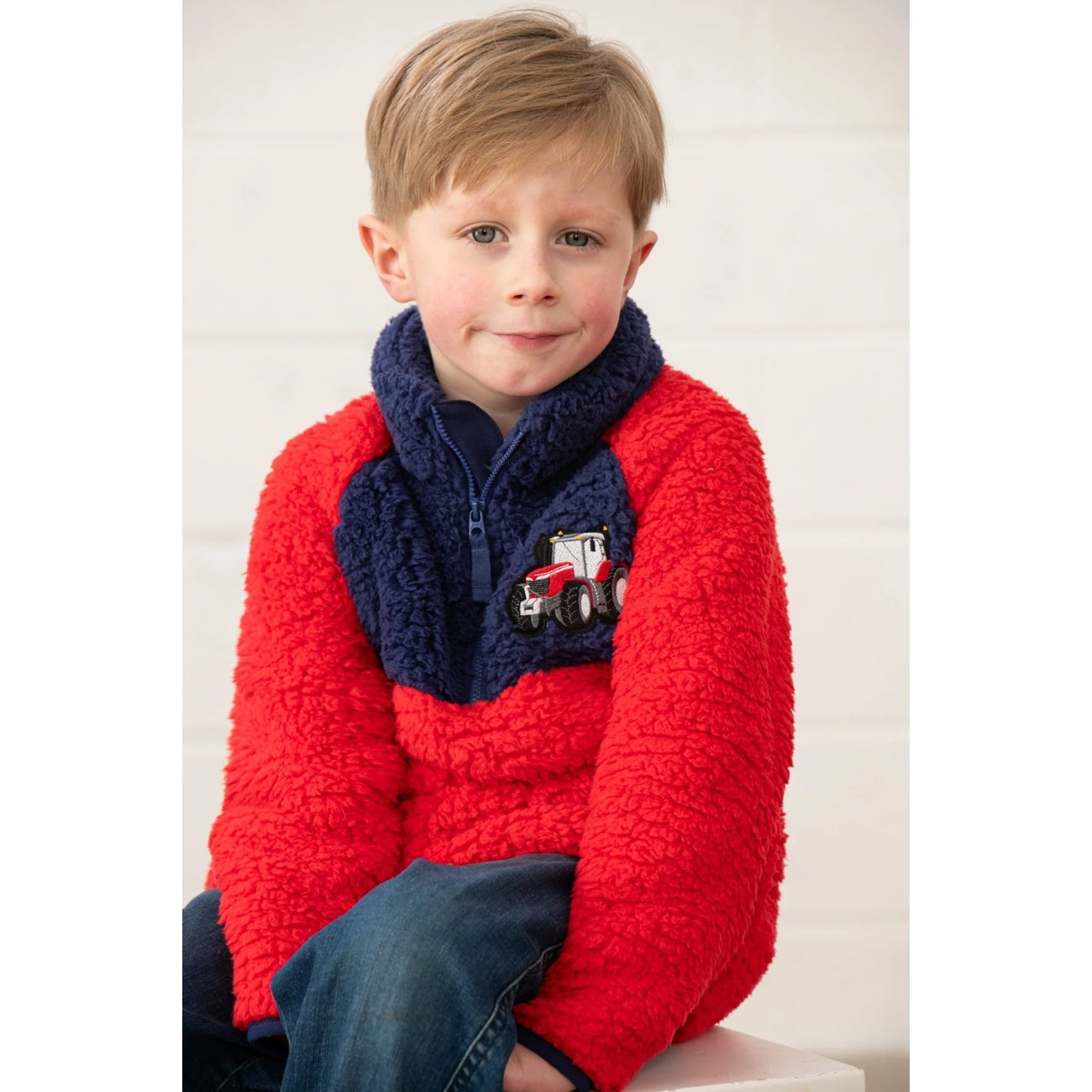 Child wearing a red Lighthouse Caden fleece jumper with a tractor design on a white background