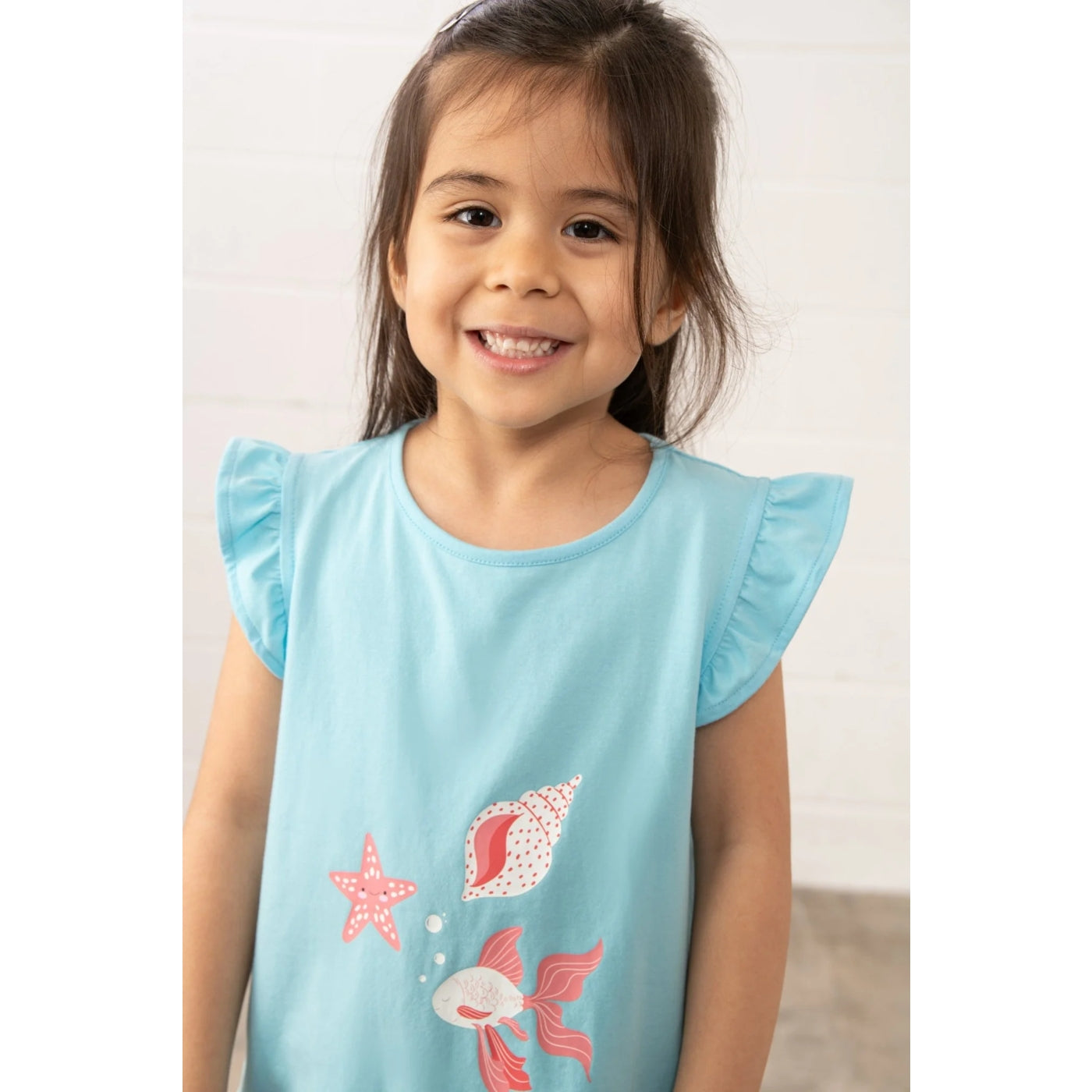 Young girl wearing a light blue Lighthouse t-shirt with sea-themed print on a plain background