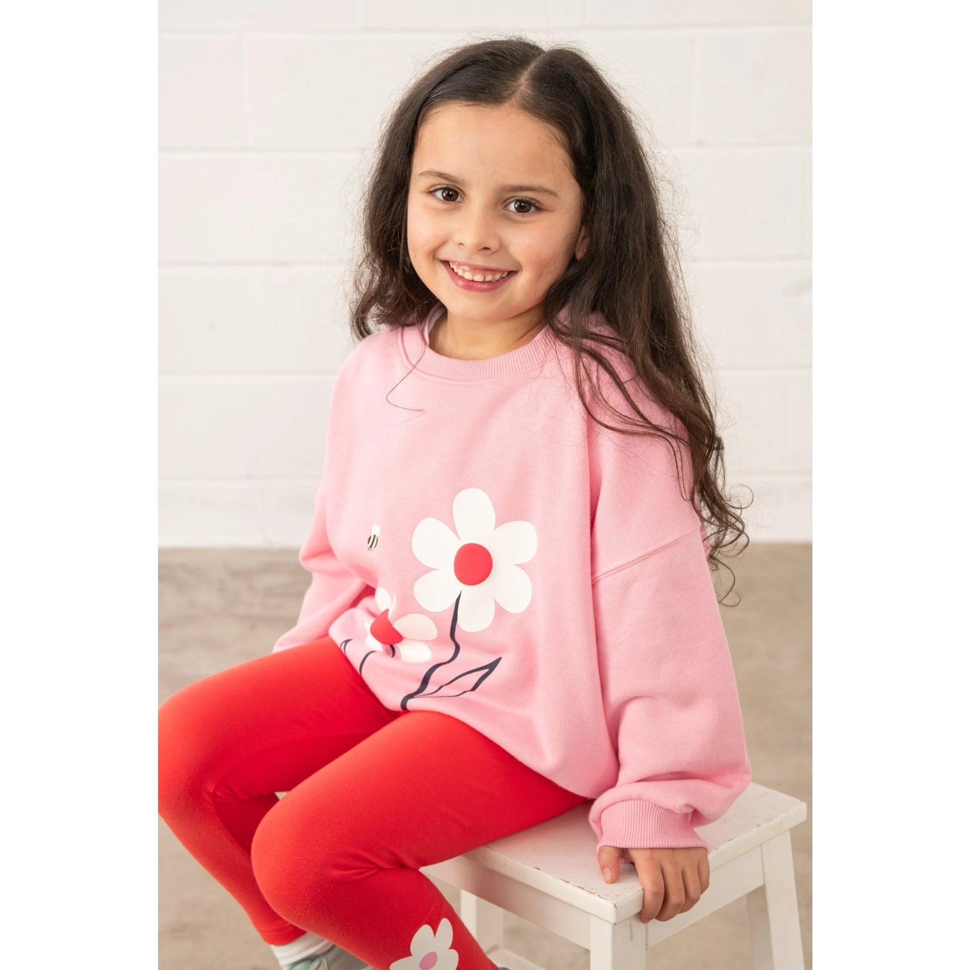 Lighthouse kids Flora sweatshirt Dusky Pink flowers worn by girl sitting on white stool smiling