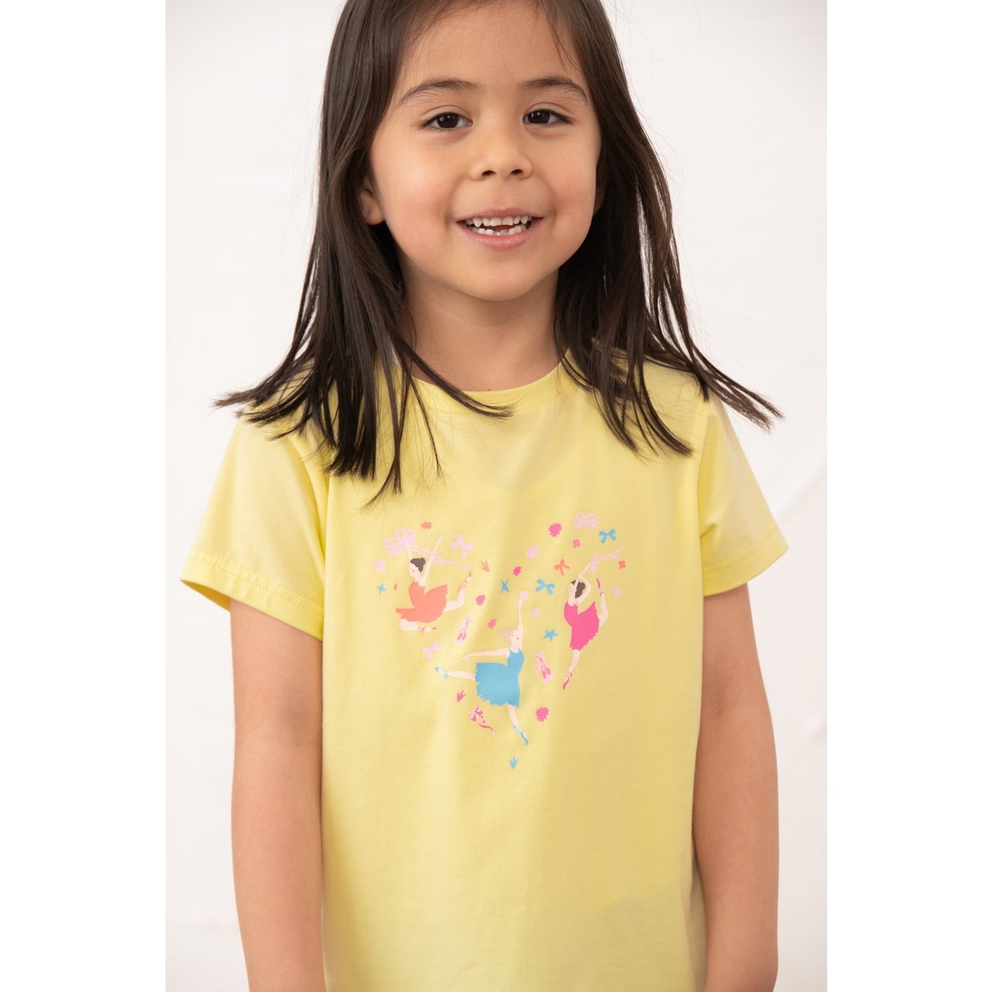 Close-up view of a girl wearing a kids Lighthouse short sleeve Causeway t-shirt in lemon yellow, featuring a heart shape ballerina print on the front.
