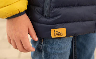 Close-up of Lighthouse kids padded coat navy yellow label on navy blue padded coat sleeve and hem