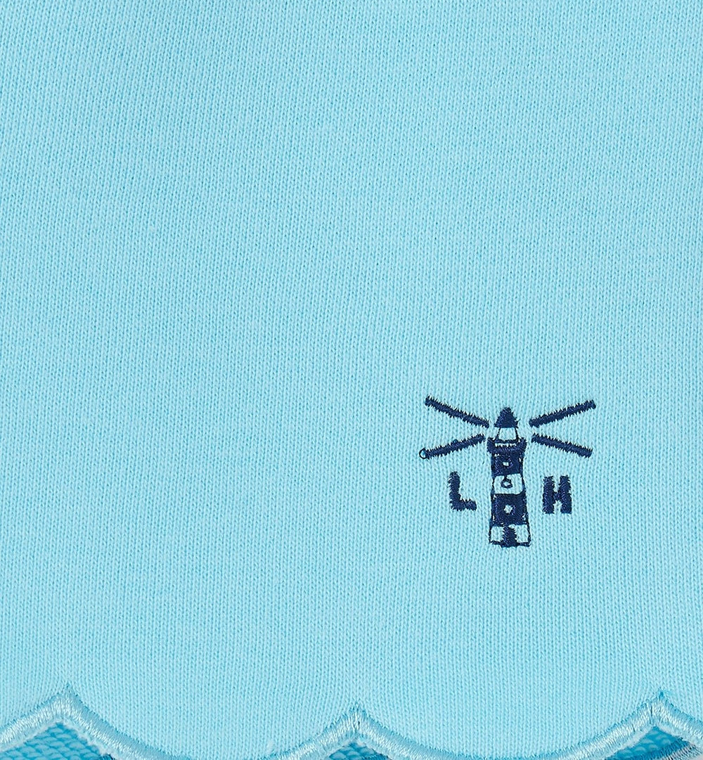 Close-up of Lighthouse kids shorts blue featuring embroidered navy lighthouse logo on light blue fabric