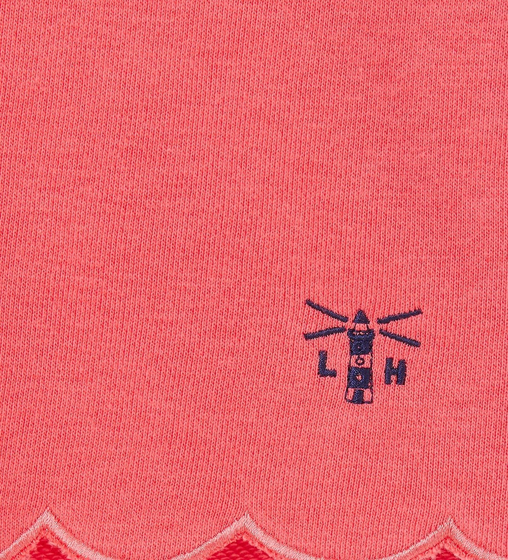 Close-up of coral fabric with scalloped edge and lighthouse logo on Lighthouse kids shorts coral