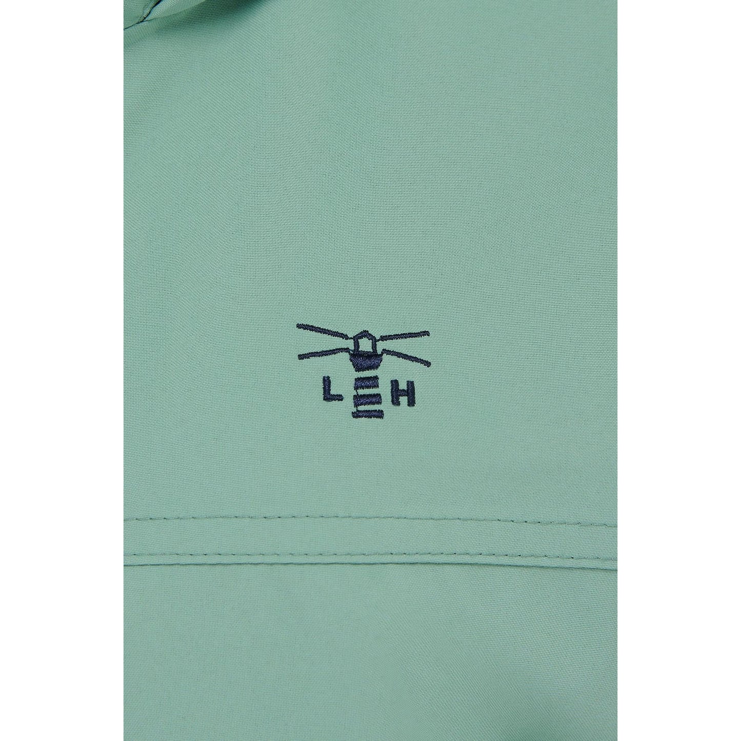 Close-up view of the green fabric with embroidered lighthouse logo of a Lighthouse waterproof Beachcomber II waterproof jacket in Basil green.