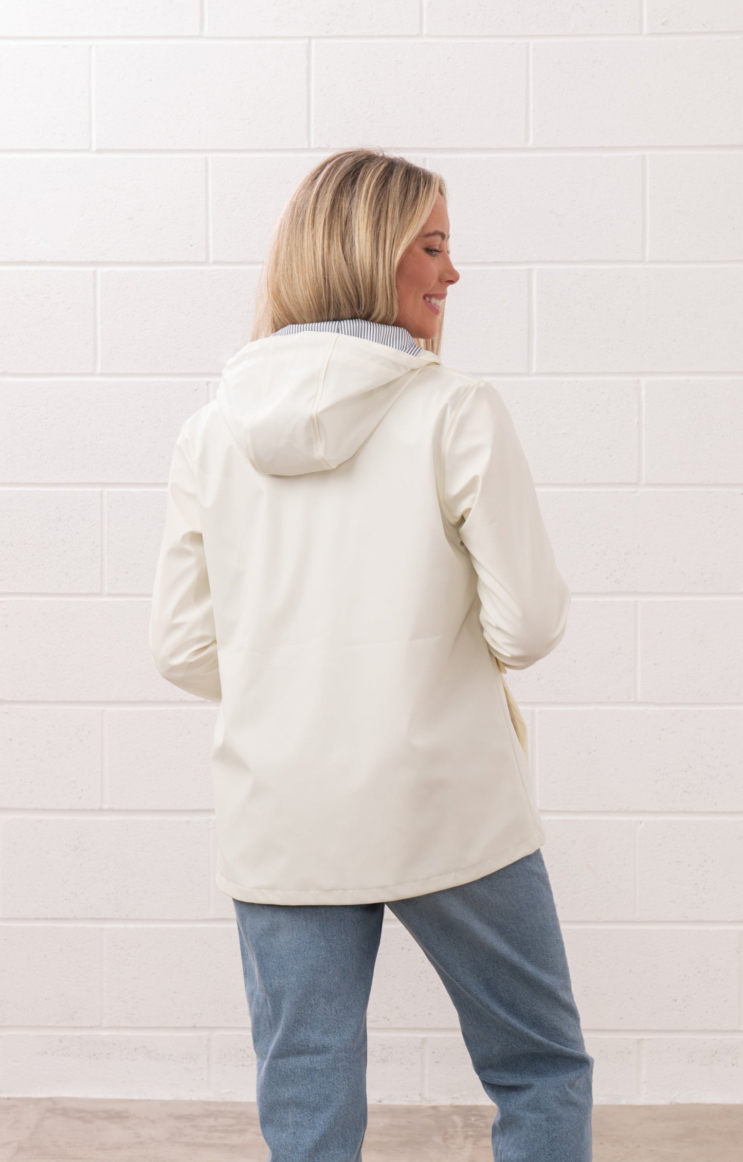 Back view of a woman wearing a white Lighthouse womens Coconut jacket with a hood and blue jeans