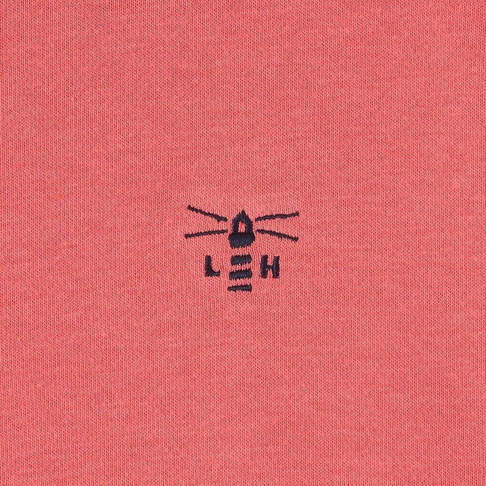 Close-up of a coral fabric with a black embroidered Lighthouse logo.
