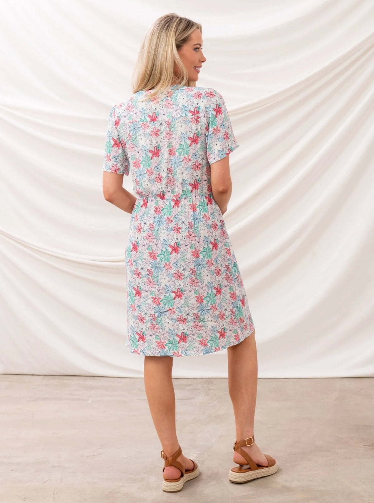 Back view of a woman wearing a Lighthouse womens floral dress with short sleeves and a colorful flower pattern