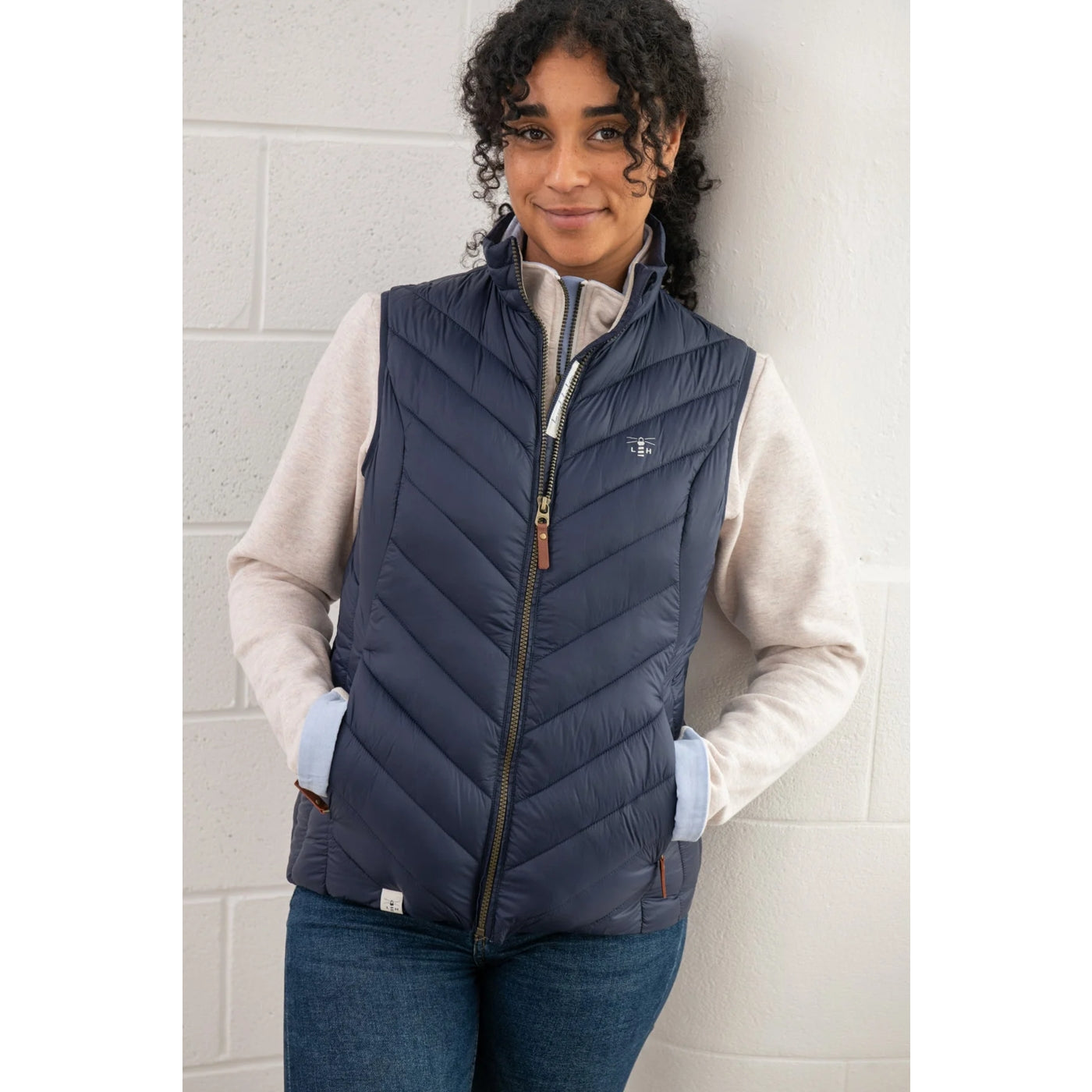 Woman wearing a Lighthouse Laurel navy puffer vest over a light-coloured shirt against a tiled wall.