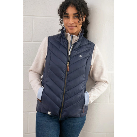 Woman wearing a Lighthouse Laurel navy puffer vest over a light-coloured shirt against a tiled wall.