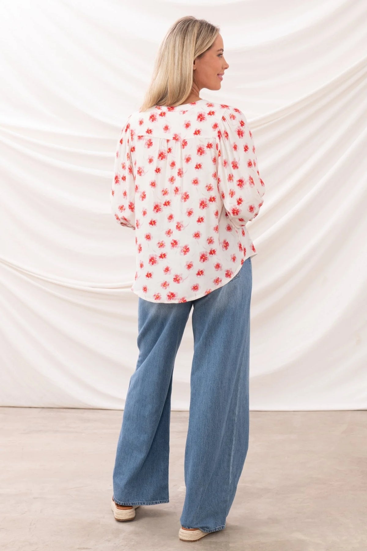 Back view of a woman wearing a white blouse with red floral print and blue jeans Lighthouse womens Lola blouse