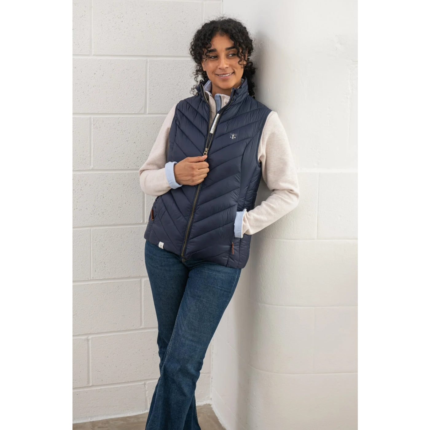 Woman wearing a Lighthouse Laurel navy puffer gilet against a light grey tiled wall