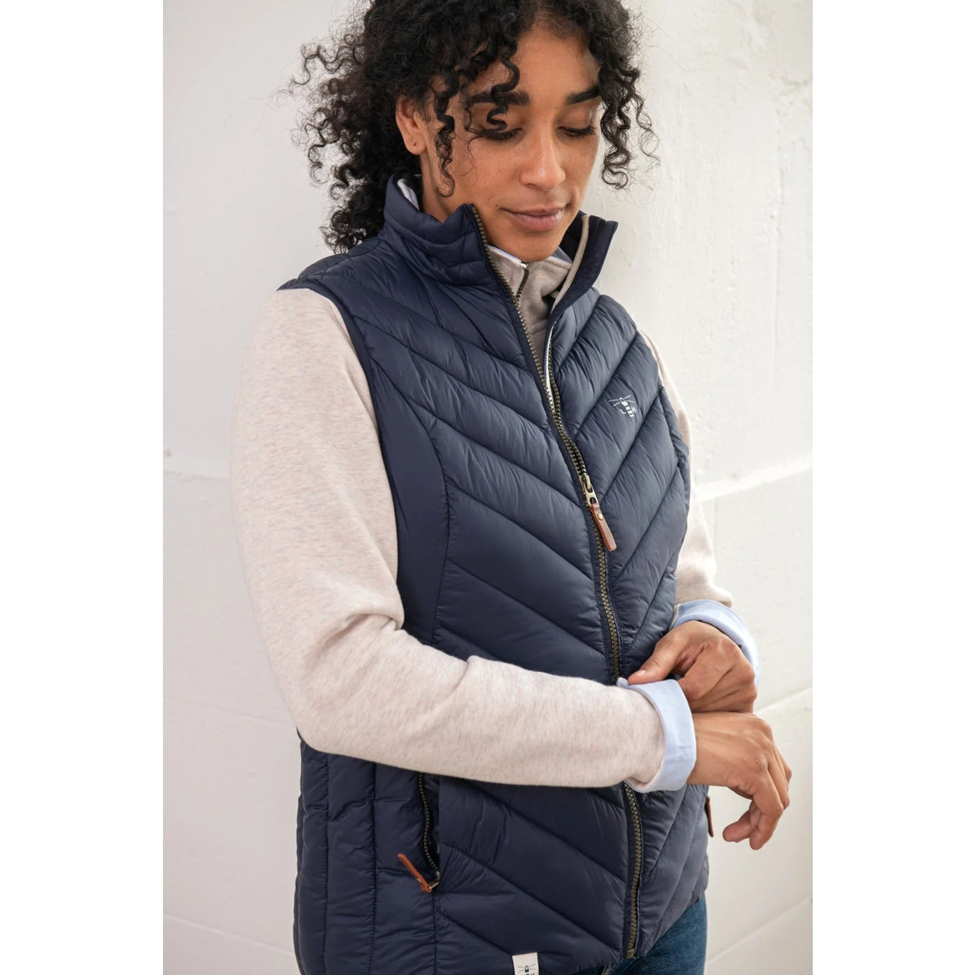 Woman wearing a navy blue Lighthouse puffer gilet over a light grey shirt against a white background