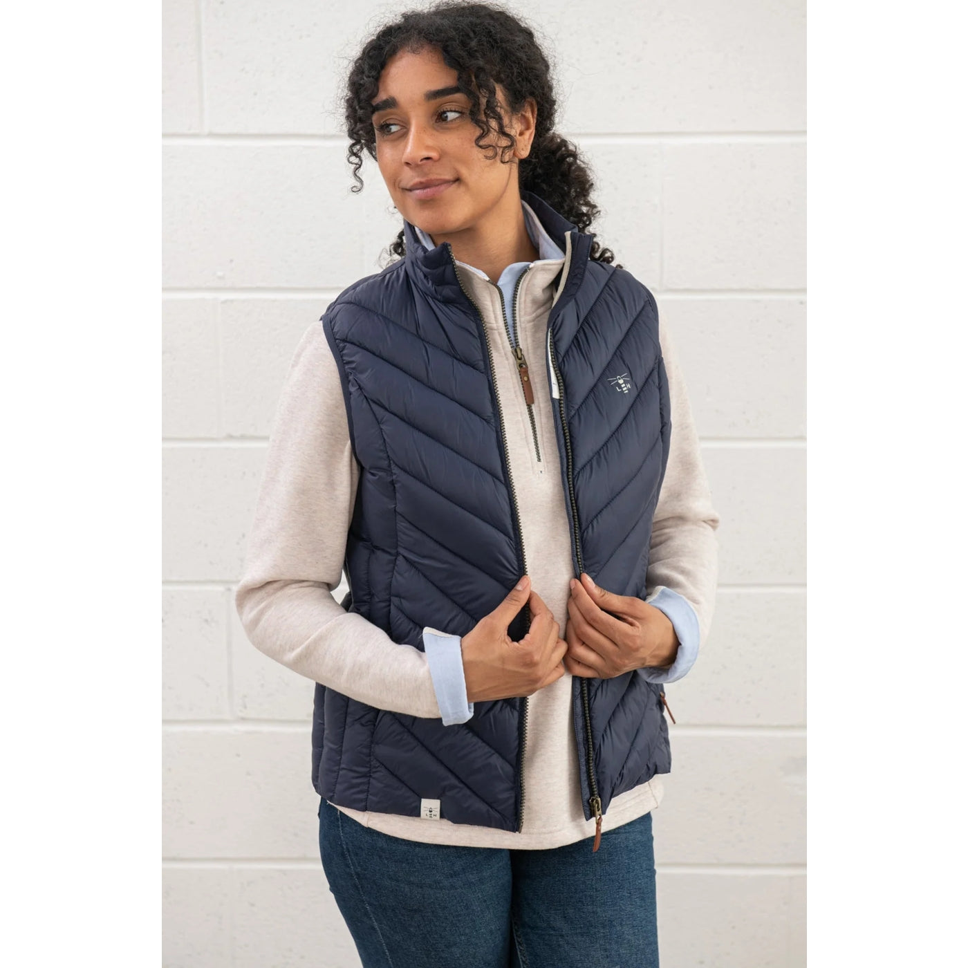 Woman wearing a navy Lighthouse Laurel puffer gilet over a white shirt against a white wall