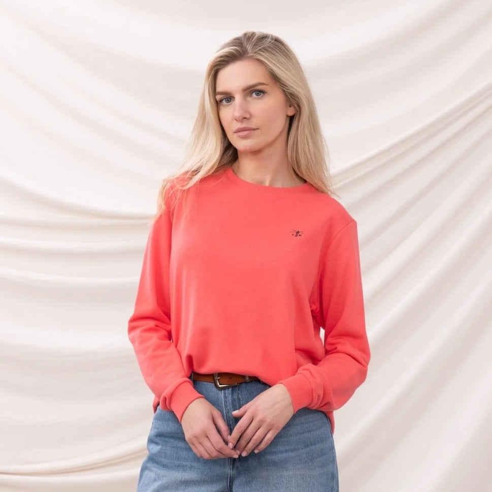 Woman wearing a Lighthouse coral Seaside sweatshirt with a small chest logo against a white background
