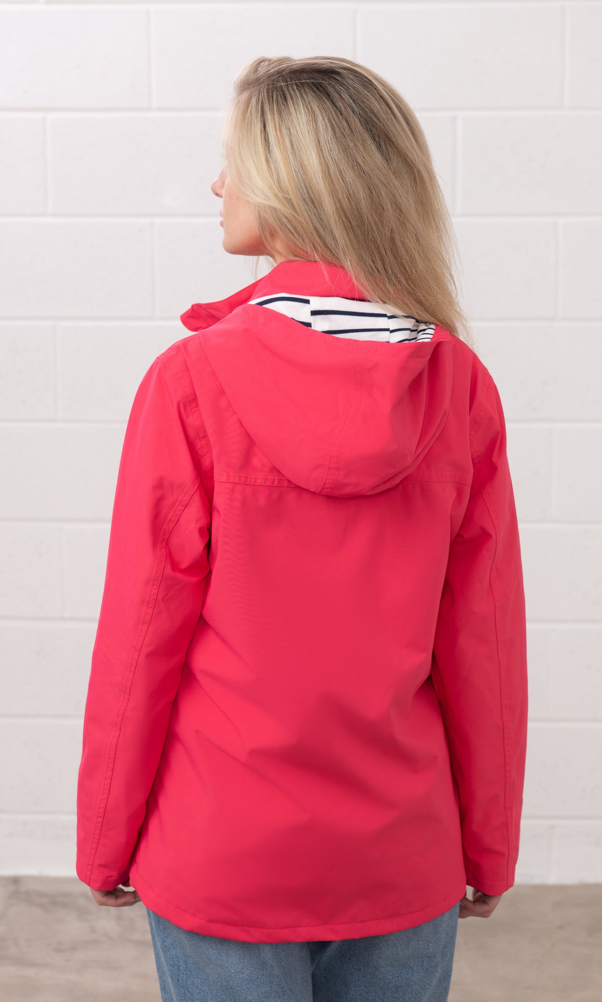 Back view of a woman wearing Lighthouse womens waterproof jacket raspberry with hood and striped inner lining