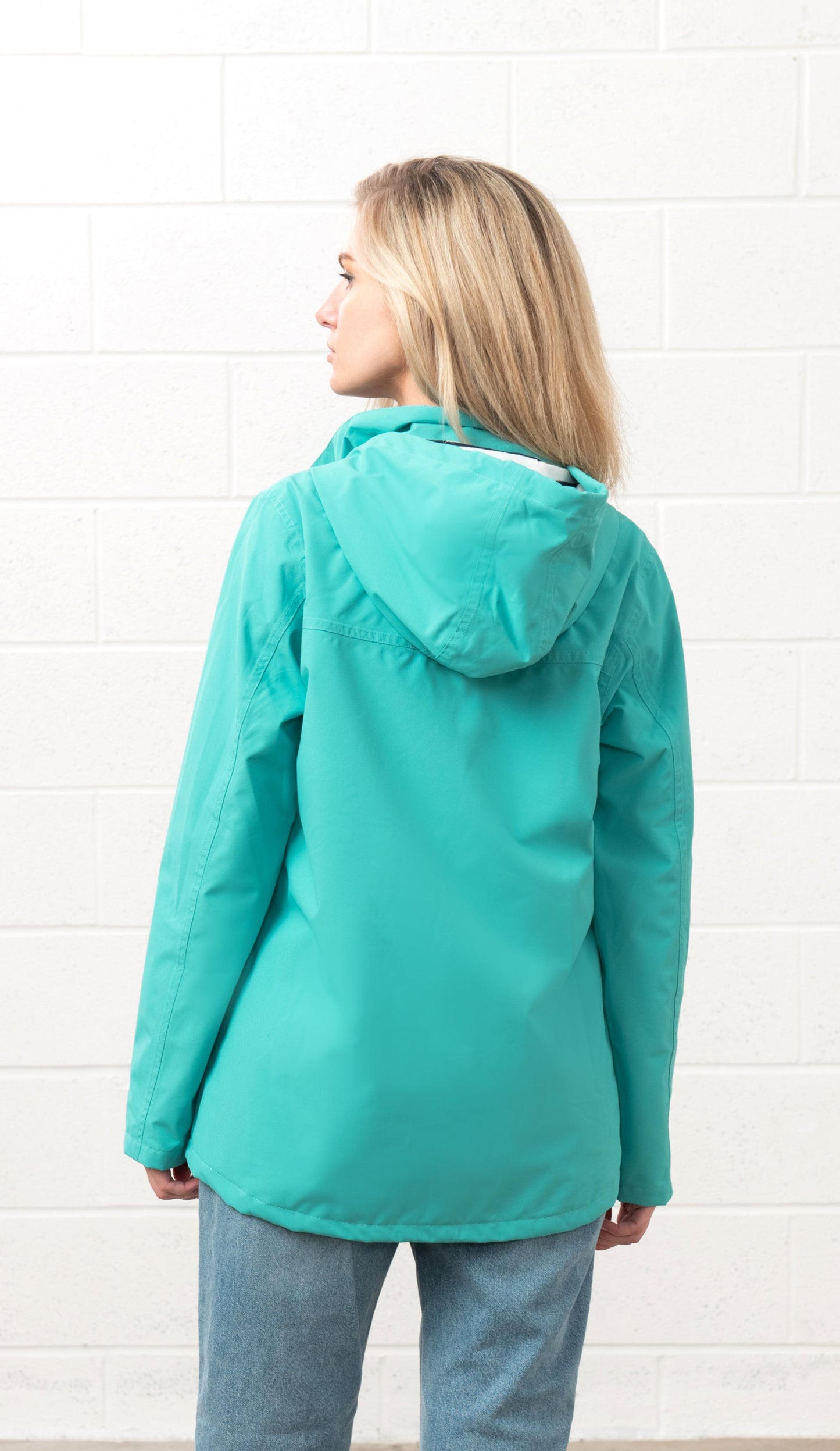 Lighthouse womens waterproof jacket teal with hood shown from the back on a model in casual jeans