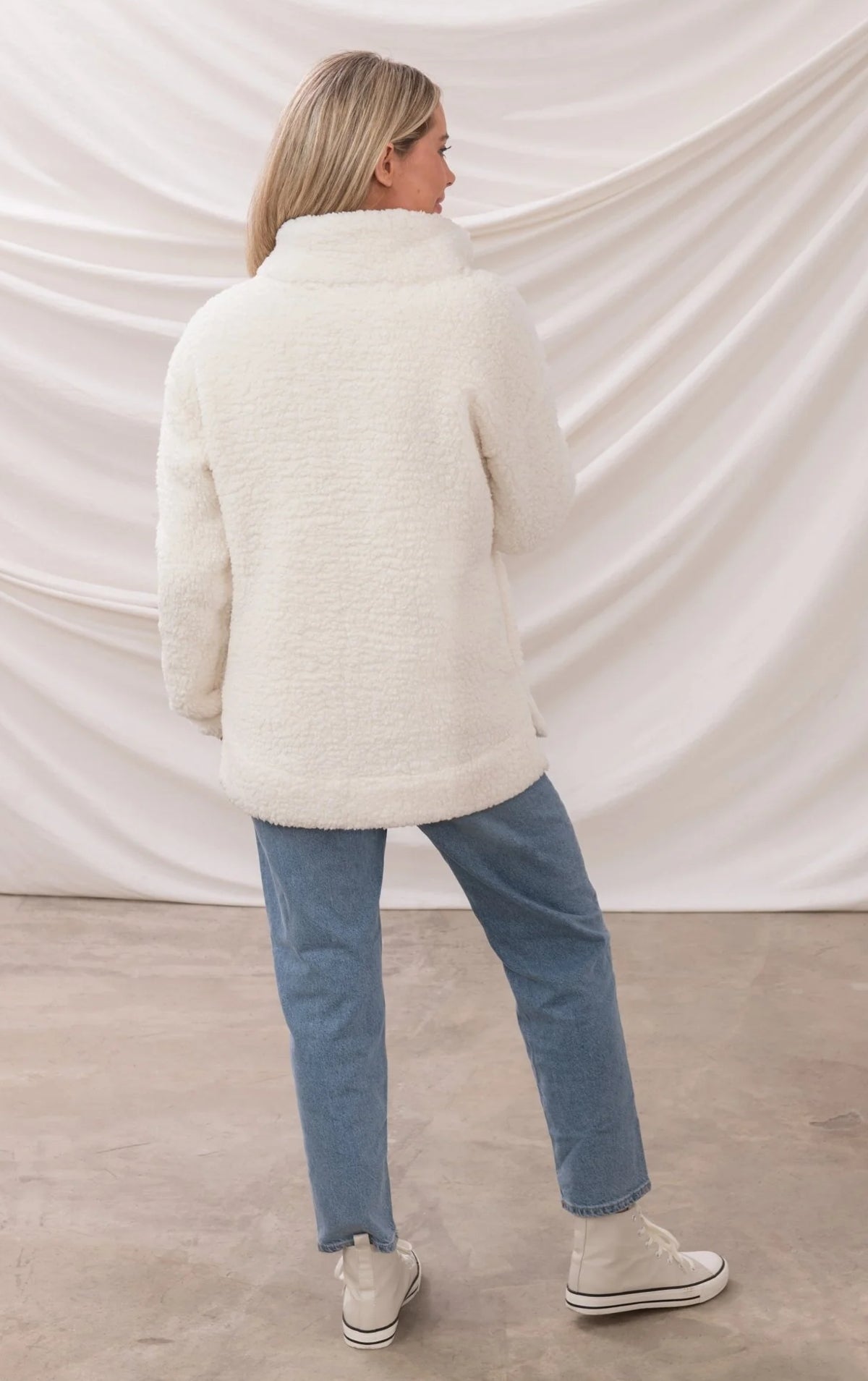Back view of woman wearing white Lighthouse womens zip fleece with high collar and blue jeans