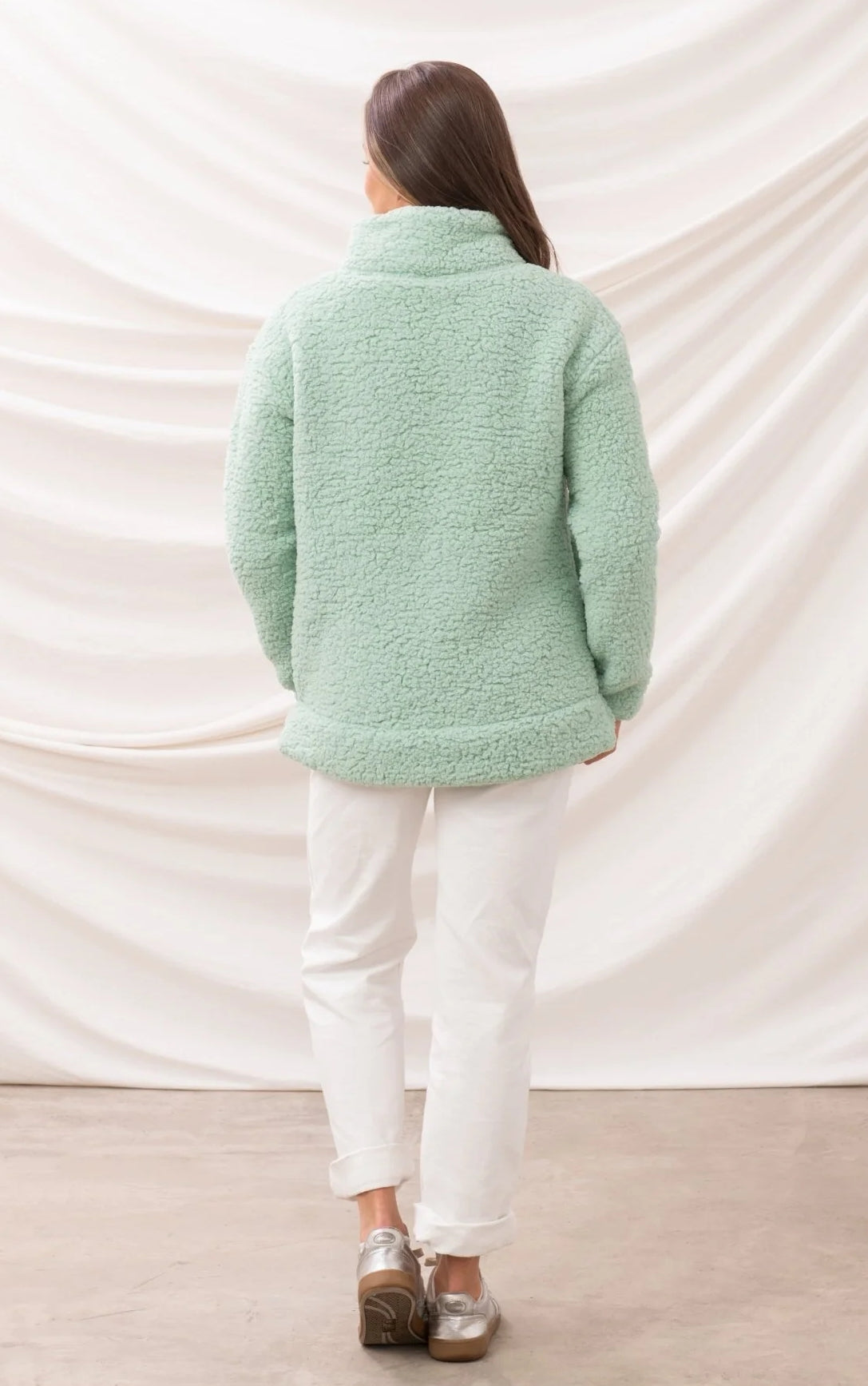 Back view of a woman wearing a light green Lighthouse womens zip neck fleece with white pants