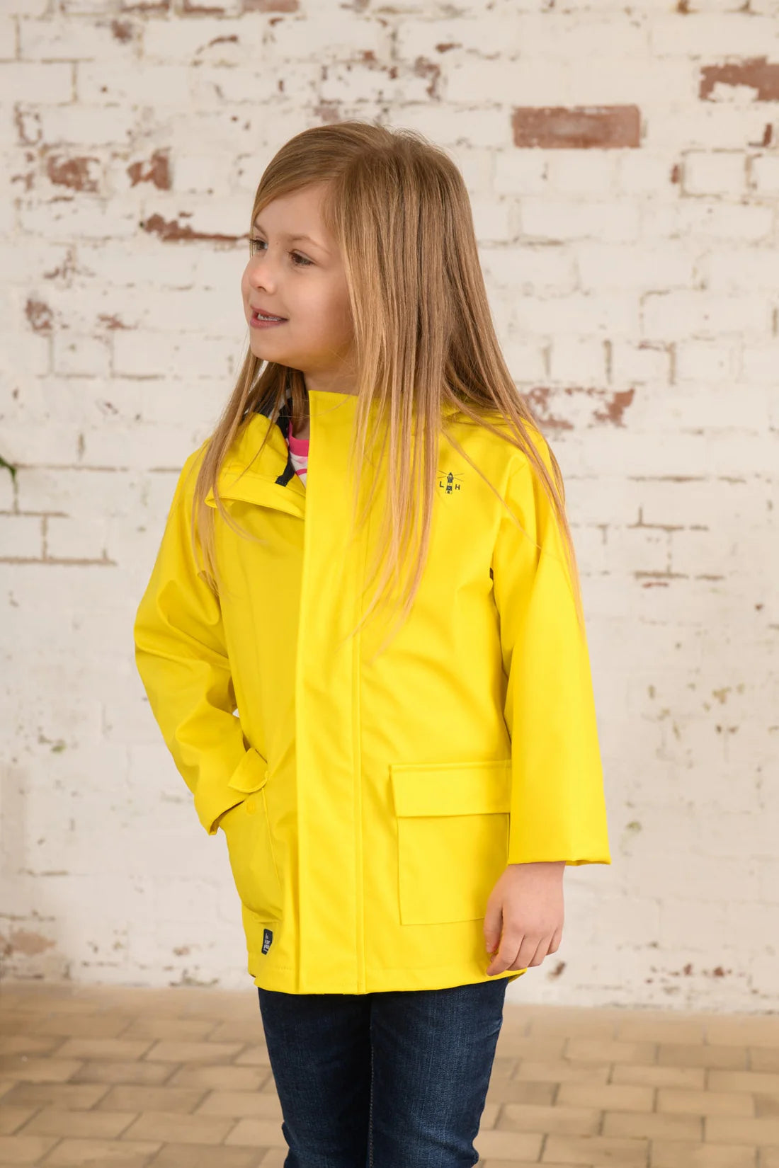 Child wearing a yellow Max raincoat from Lighthouse with a hand in one of the front pockets.
