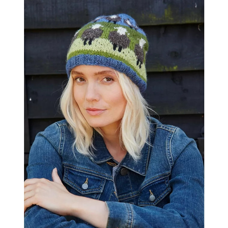 Woman wearing a knitted Pachamama hat with sheep pattern against a wooden background
