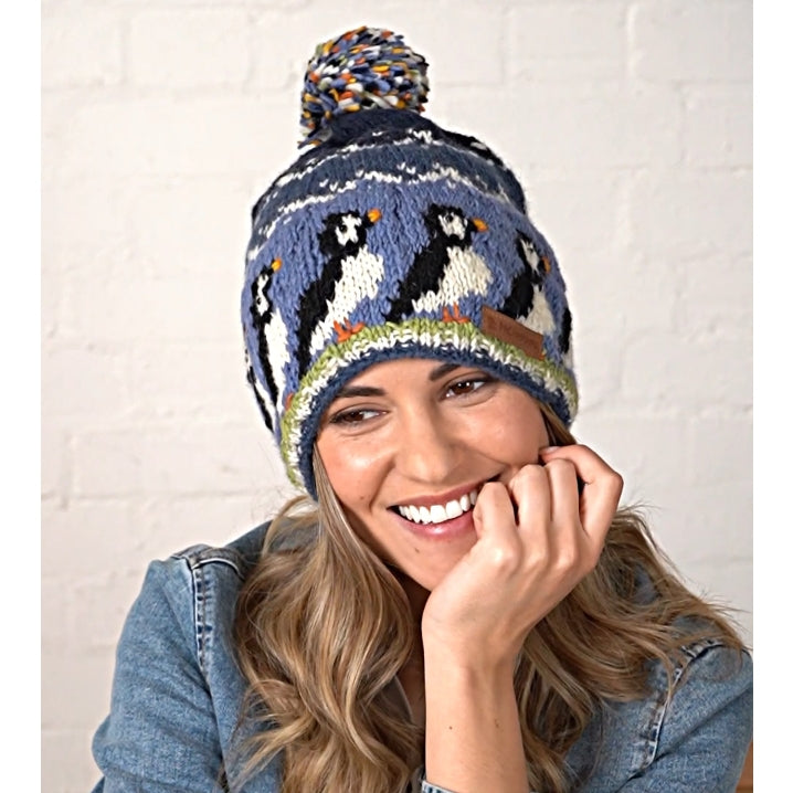 Woman wearing a blue knitted Pachamama hat with puffin design against a white background