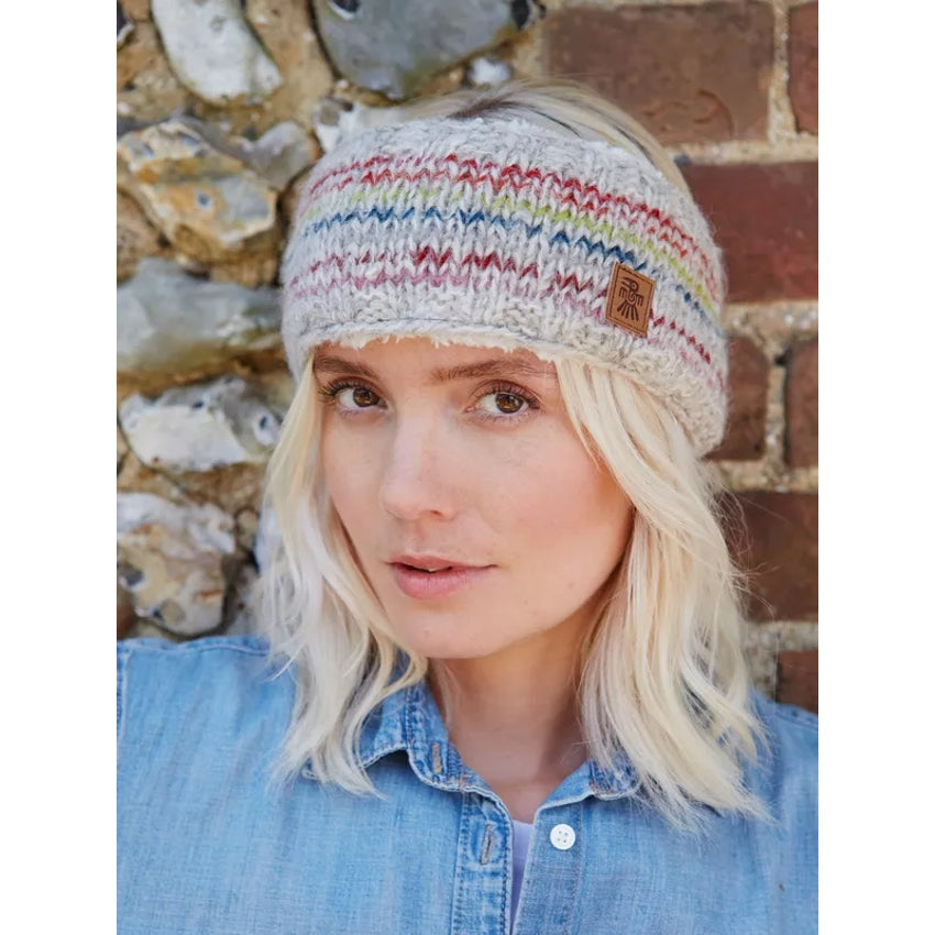 Woman wearing a colourful Pachamama Langtang knitted beanie against a stone wall background