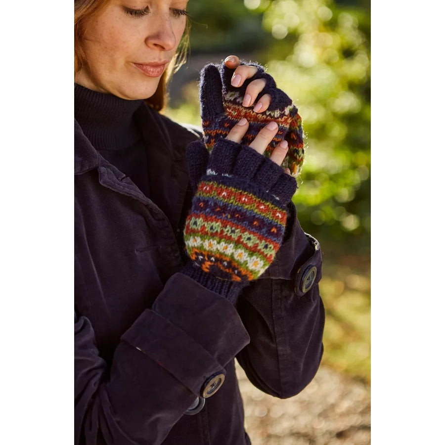 Person wearing a dark coat and colourful Pachamama knitted mittens outdoors.