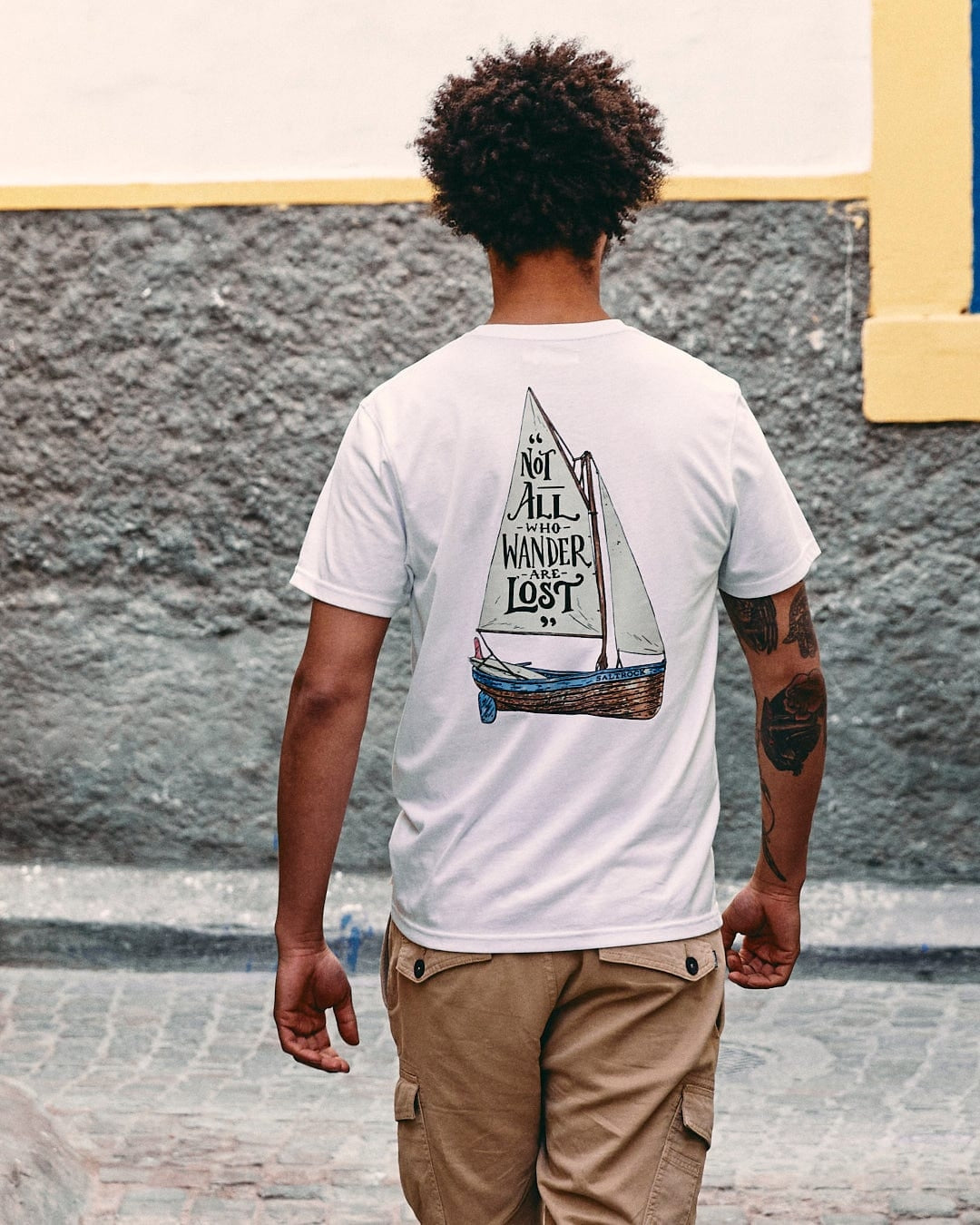 Back view of a man wearing a white Saltrock mens lost ships tee with a sailboat graphic and quote