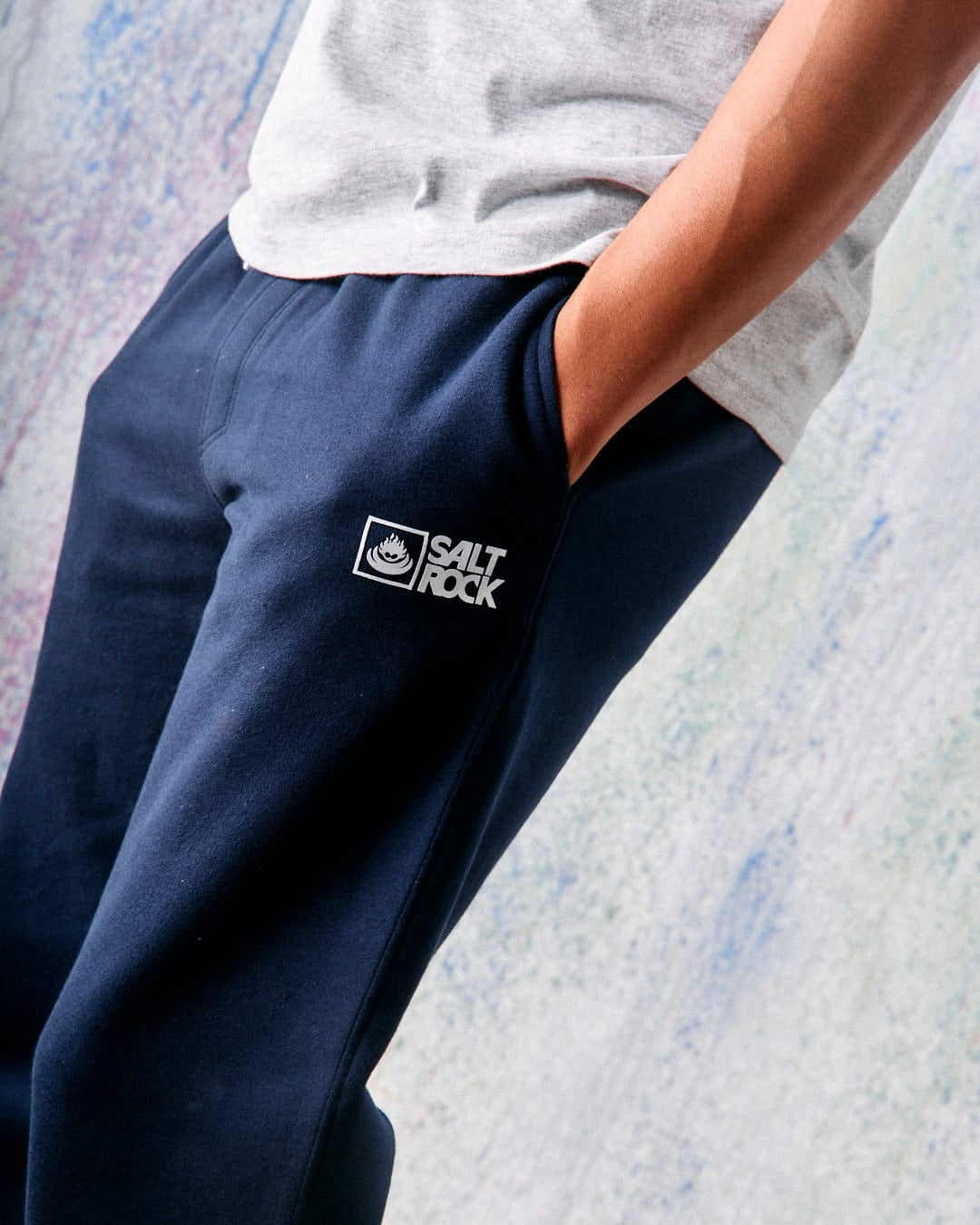 Side view of a man wearing a pair of mens Saltrock original jogger seat trousers in blue marl with a white logo and hip pockets