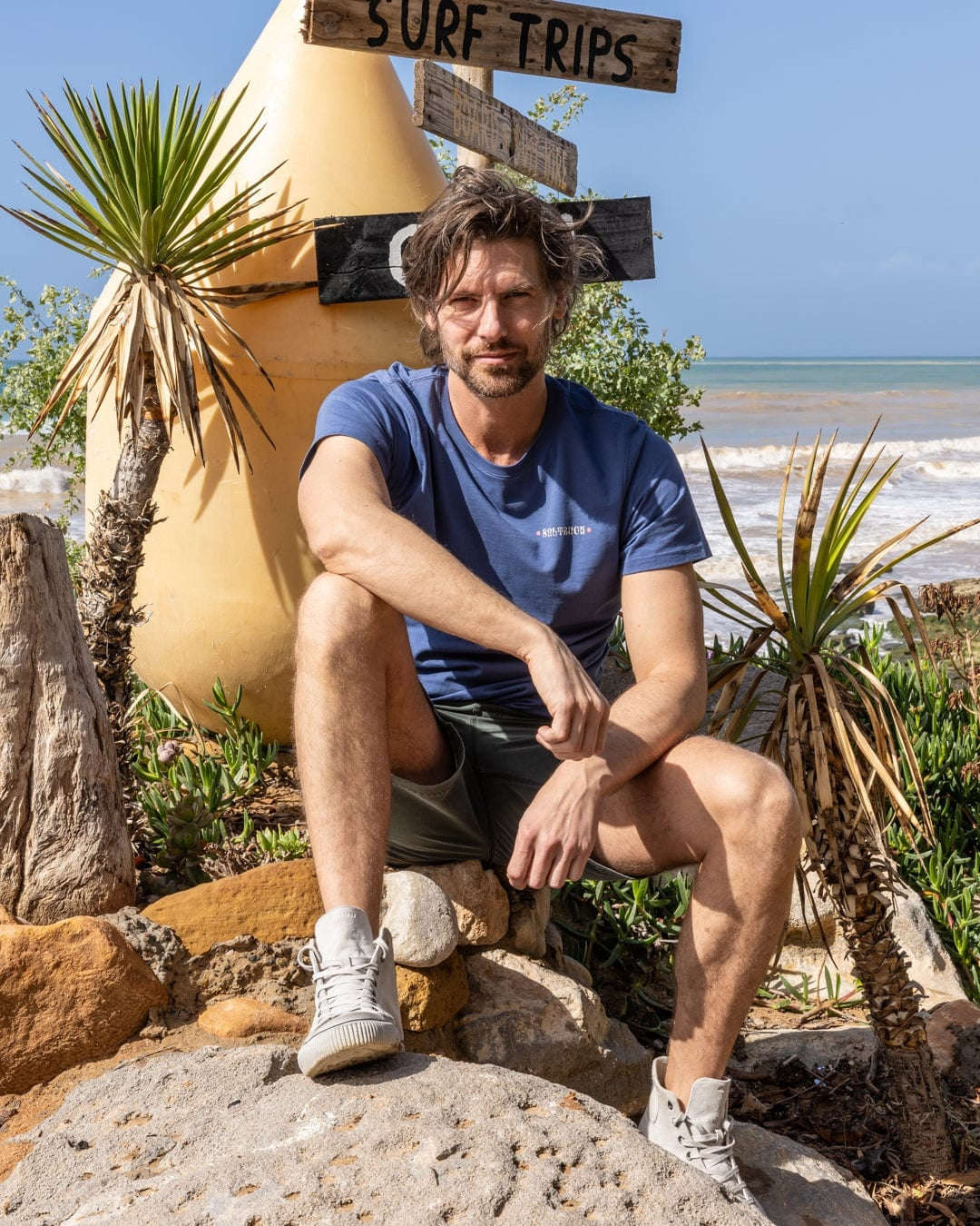 Saltrock mens t-shirt blue on model sitting outdoors by the beach with surf-themed decor