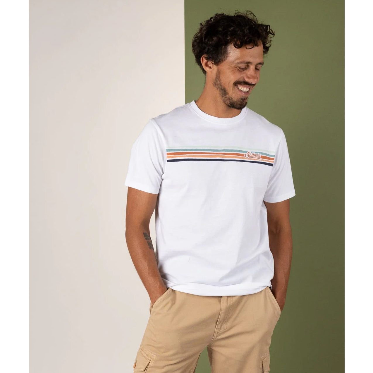 Man wearing a white Saltrock t-shirt with horizontal stripes on the chest, against a green and beige background