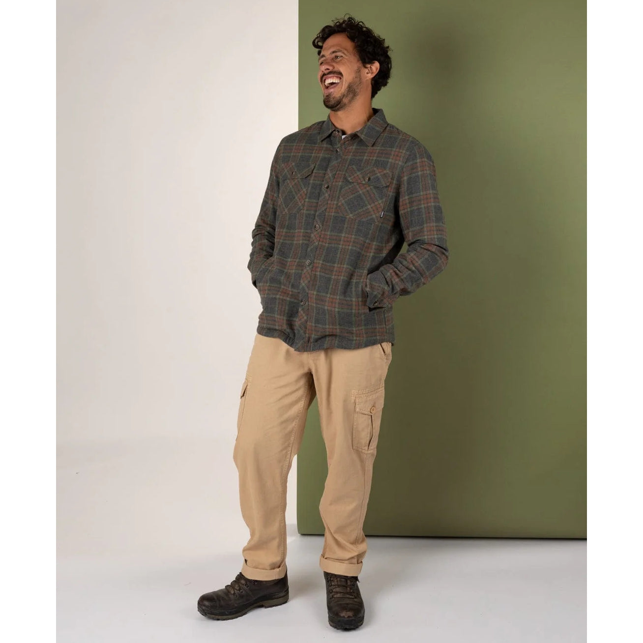Man wearing a Saltrock Woody sherpa lined grey shirt and beige pants against a green wall.