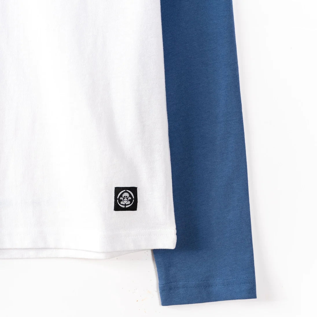 Close-up of a white Saltrock kids t-shirt with a blue sleeve and a small black logo on a white background