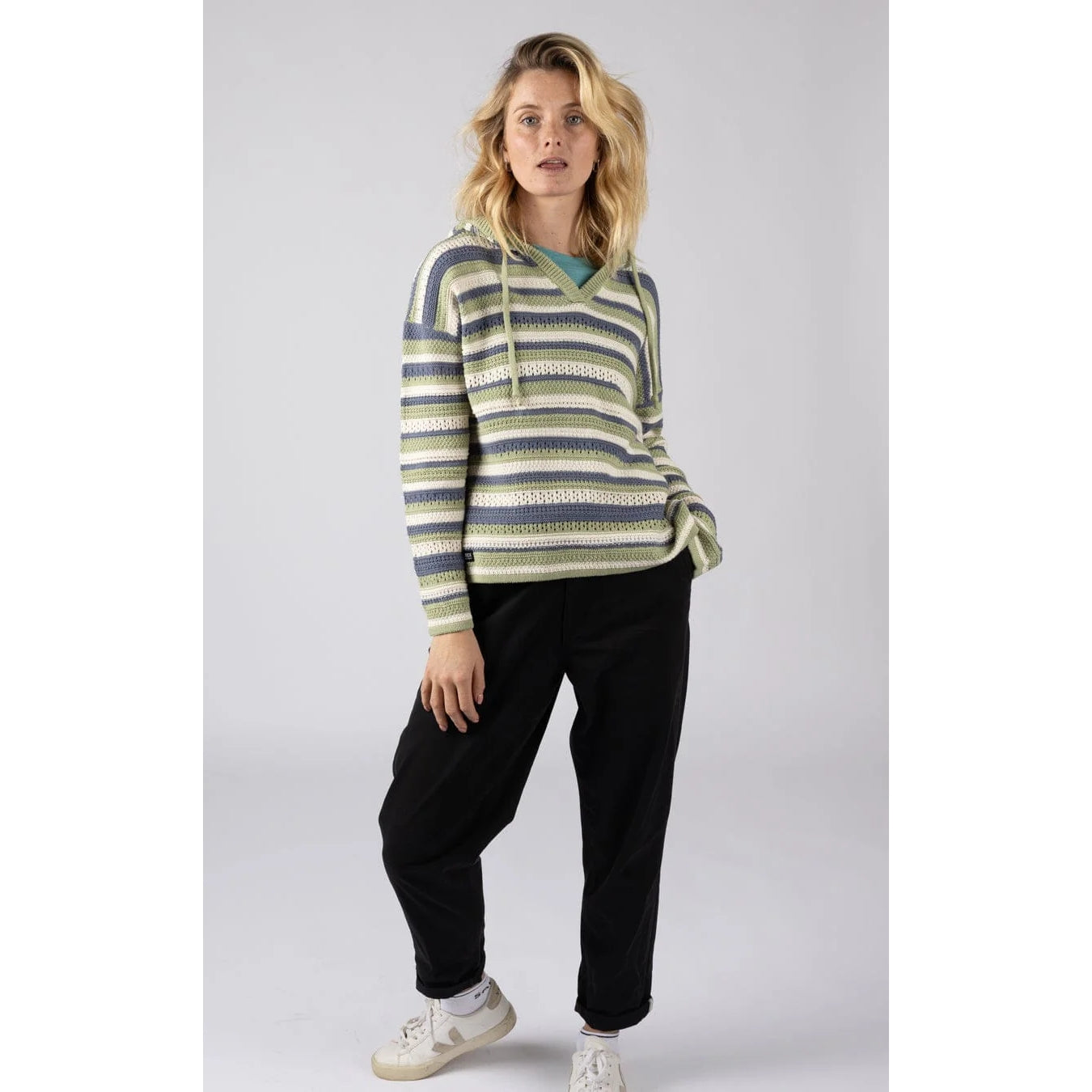 Woman wearing a striped Saltrock Aurelia knitted hoodie in green, blue and white with black pants