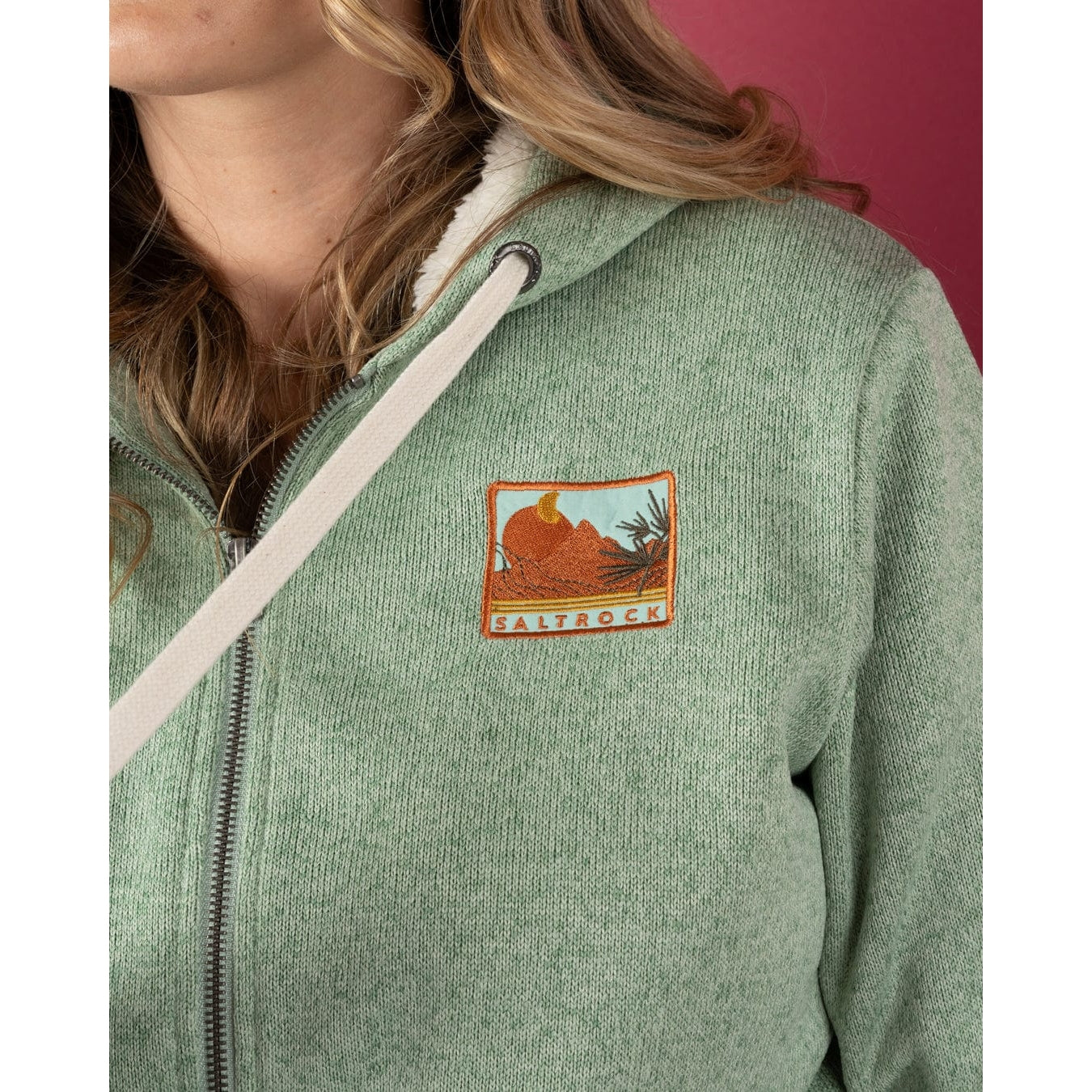 Green Saltrock womens hoodie with a logo on the chest against a pink background