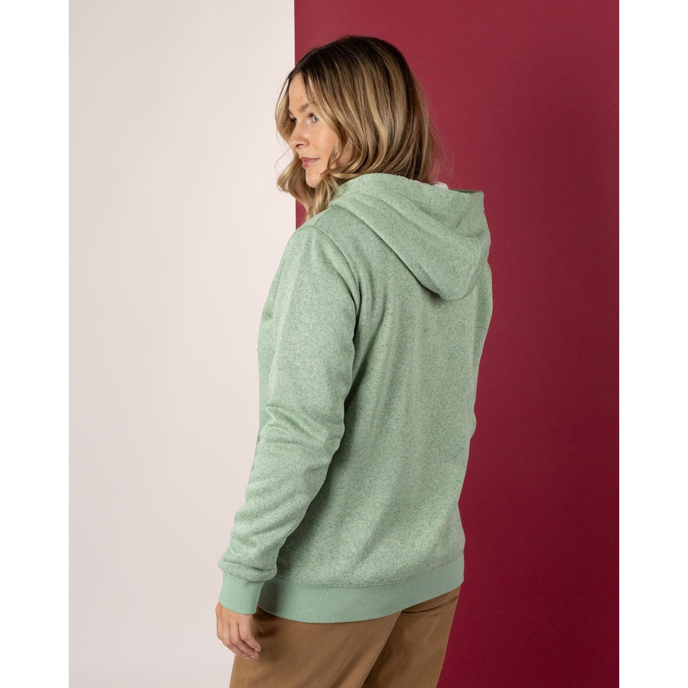 Woman wearing a green Saltrock hoodie standing against a red and white wall.