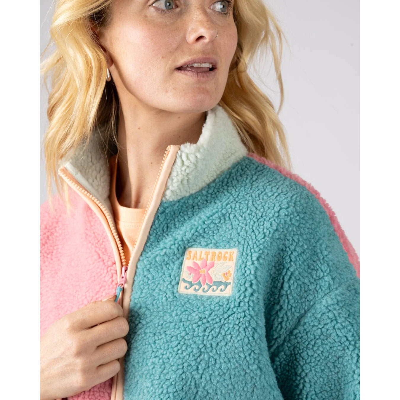 Woman wearing a Saltrock Emery Wave fleece jacket in pink, teal and turquoise with a logo patch